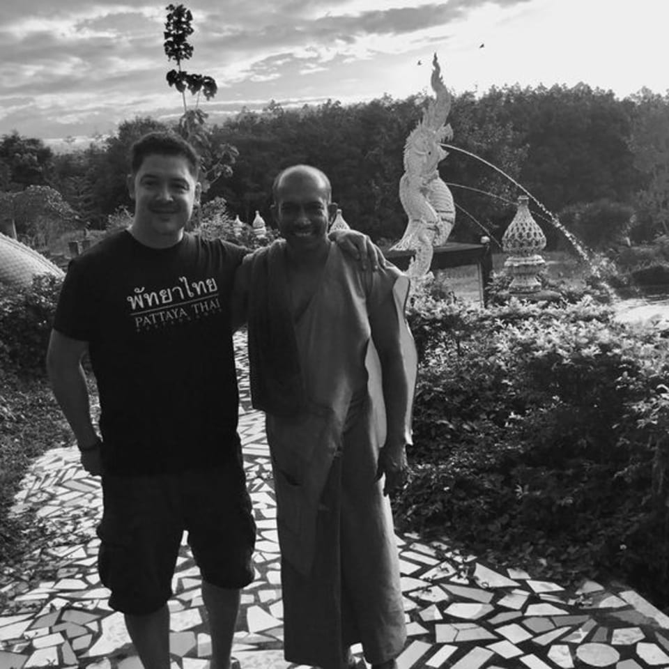 Man in Pattaya Thai shirt with another man in traditional Thai clothing on a mosaic path.