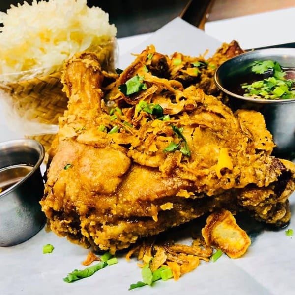 Crispy fried chicken with fried shallots, cilantro, sticky rice, and dipping sauces on a white plate.