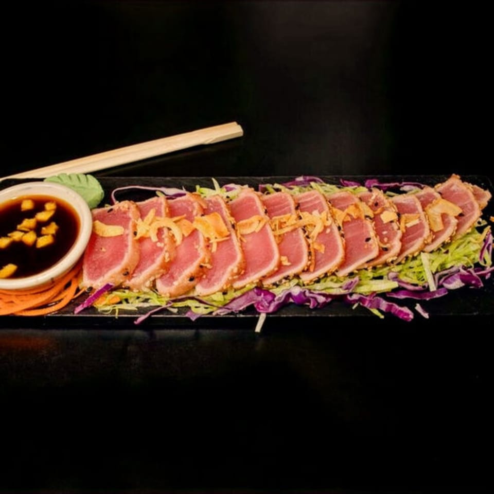 Seared tuna slices with crispy garlic, sesame seeds, shredded cabbage, and dipping sauce with chopsticks.