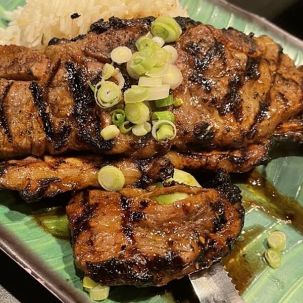 Grilled Thai BBQ pork, garnished with green onions and served with white rice on a green plate.