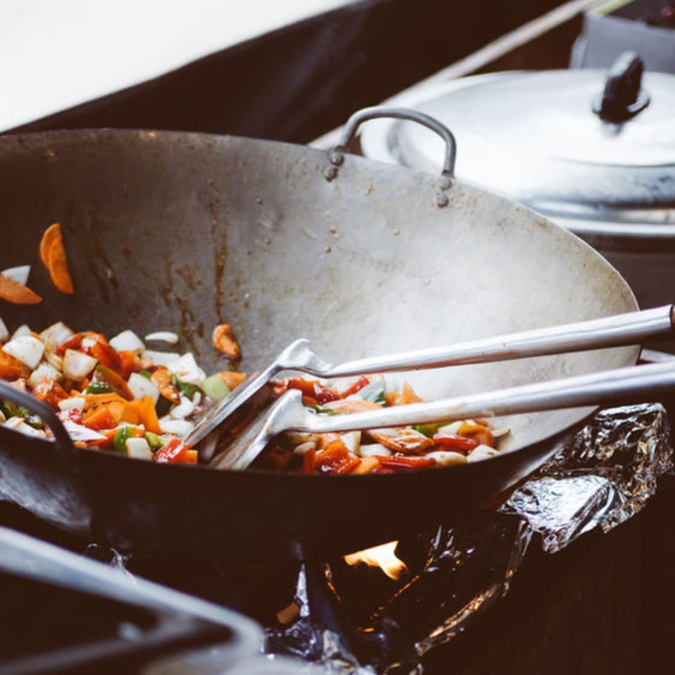 Colorful vegetables stir-frying in a large wok over an open flame at Pattaya Thai.