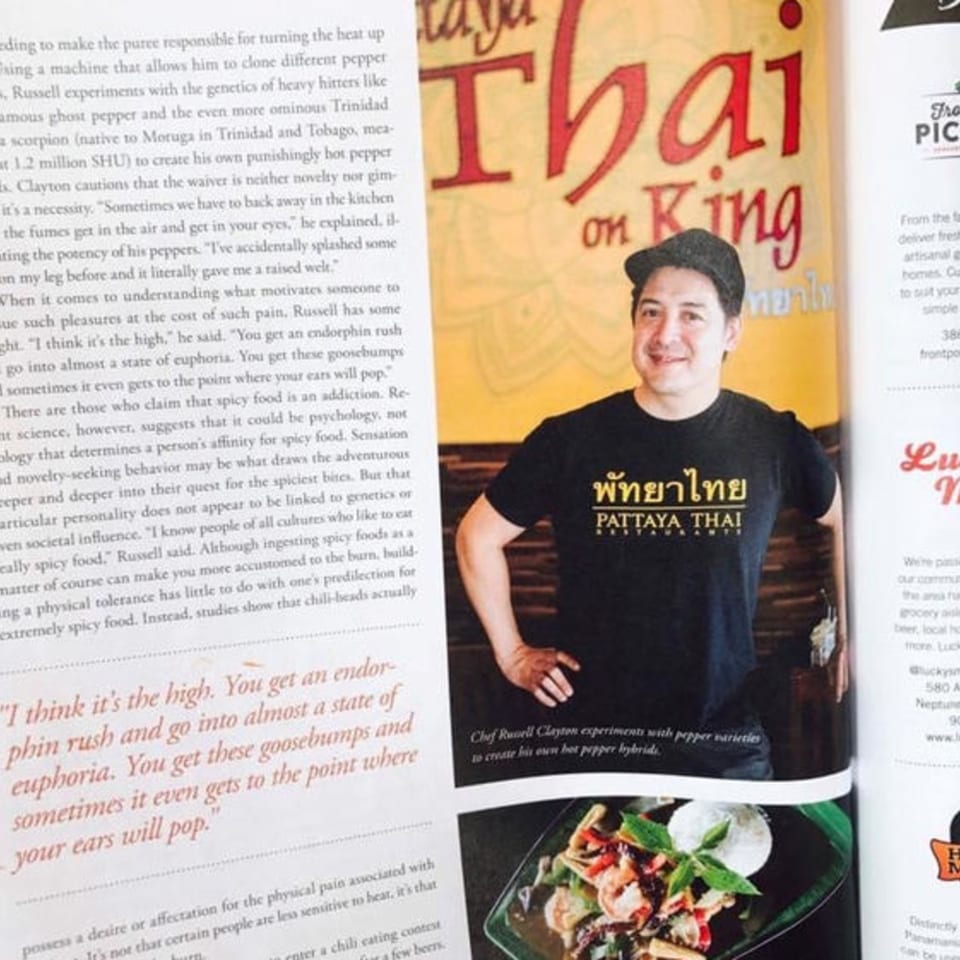A man in a black Pattaya Thai t-shirt smiles, with text about spicy food and a dish below.