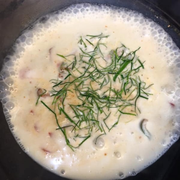 Creamy Thai curry with green herbs, possibly kaffir lime leaves, simmering in a pot.
