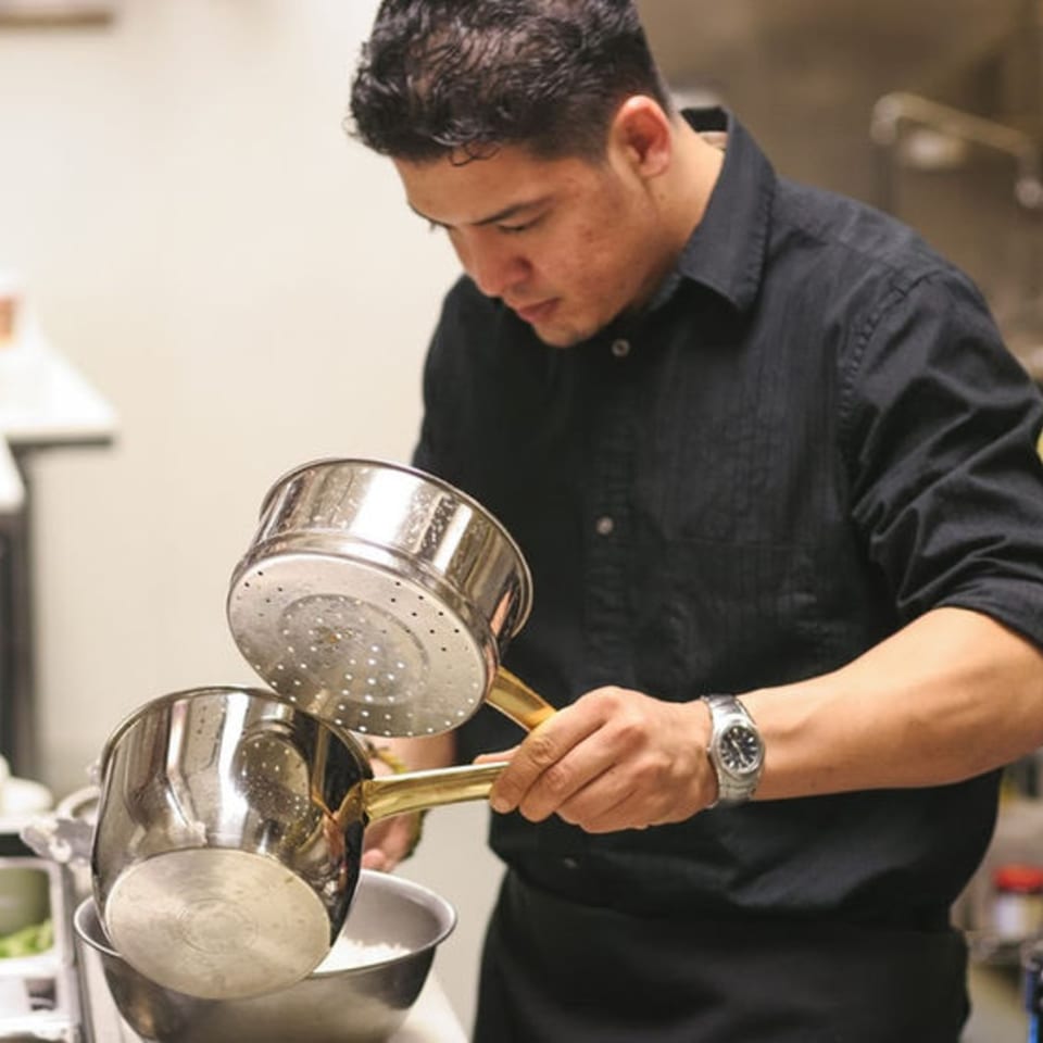Pattaya Thai chef straining rice from a pot into a metal bowl in a kitchen.