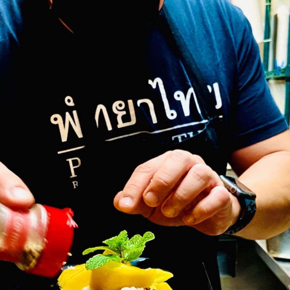 A chef in a Pattaya Thai shirt sprinkles topping on a dessert with mango and mint.