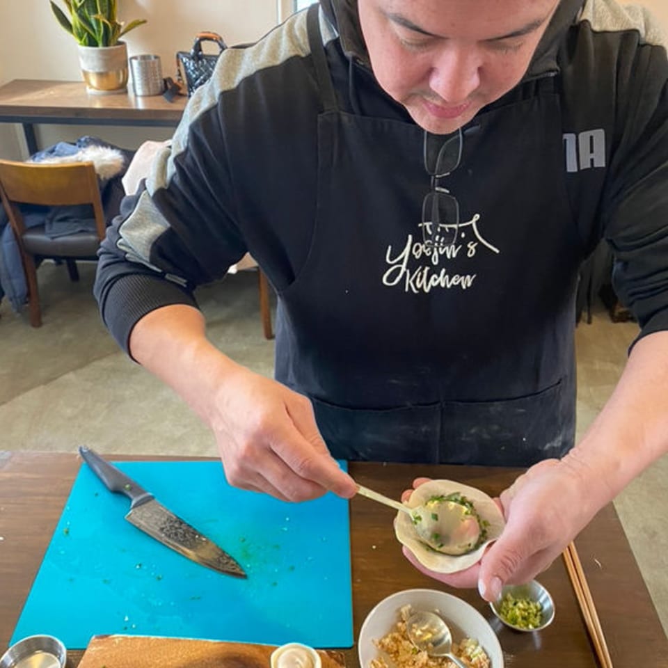A chef in a black apron fills a Thai dumpling with a spoon, preparing the dish.
