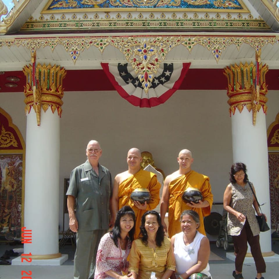 Group of people, including two monks, posing in front of a Thai temple with ornate decorations.