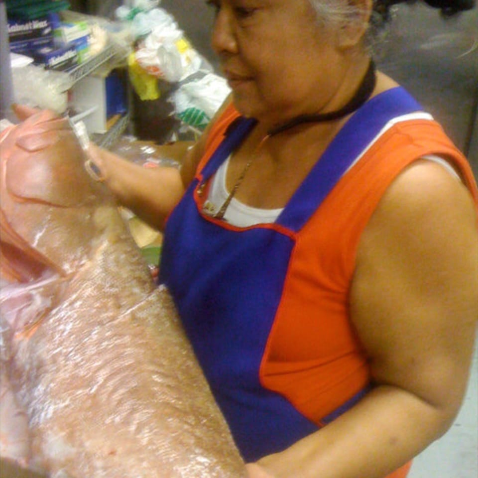 A woman in an orange and blue apron prepares a large fish for cooking.