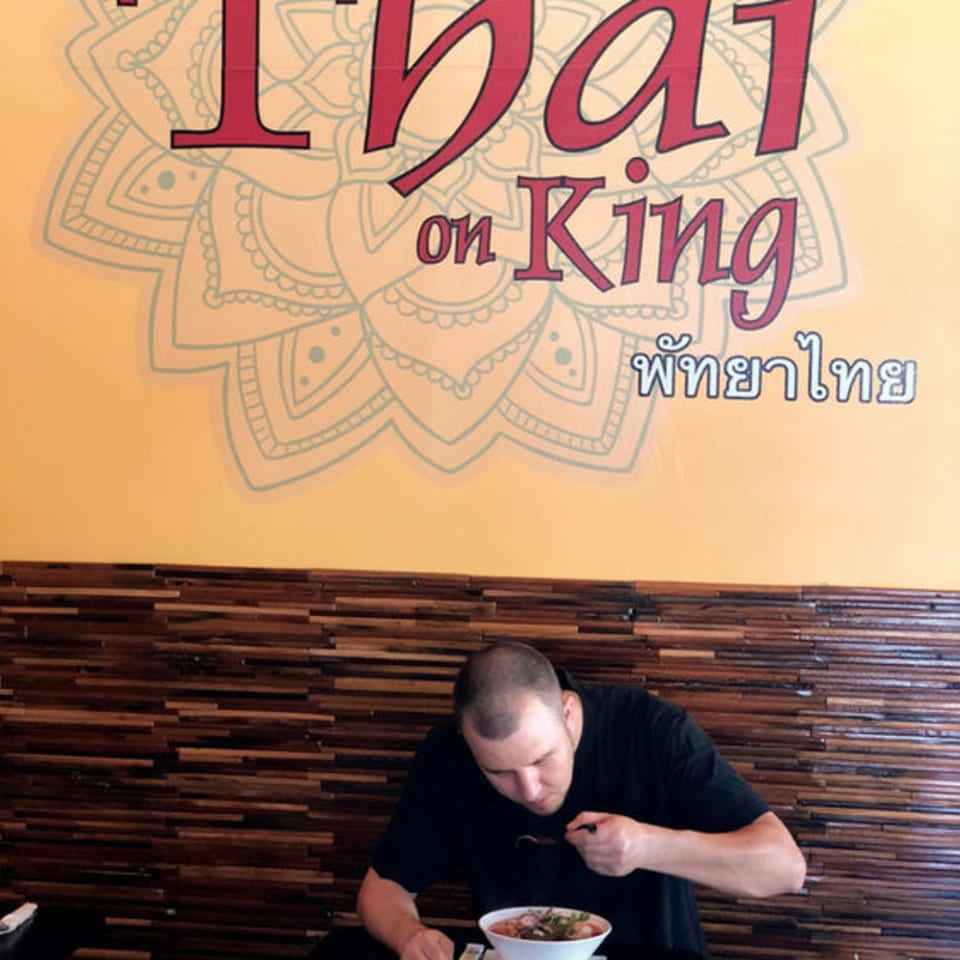 Man eating a bowl of Thai food at Pattaya Thai restaurant, with the logo visible above.