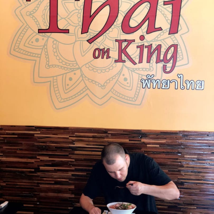 Man eating a bowl of Thai food at Pattaya Thai restaurant, with the logo visible above.