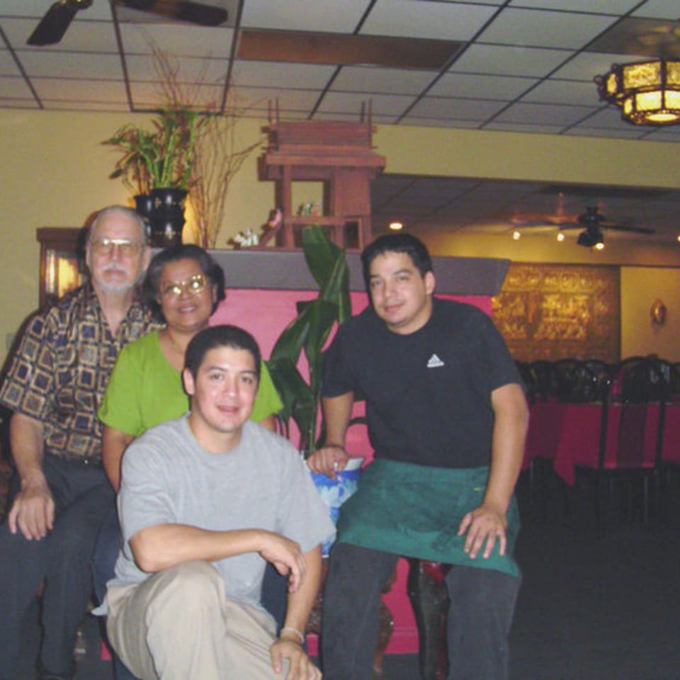 Four people, likely family, pose in a Thai restaurant dining room with traditional decor.