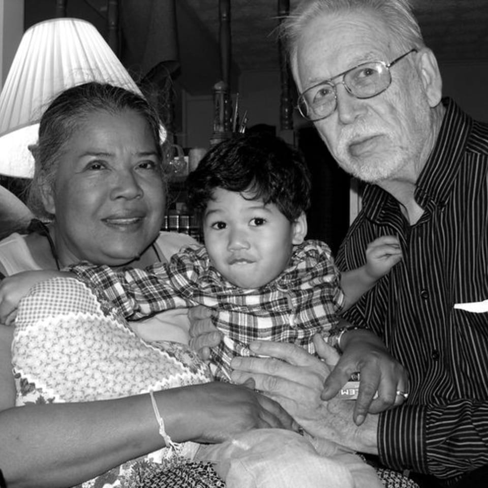 A black and white portrait of a smiling Thai woman, a young child, and an older man.