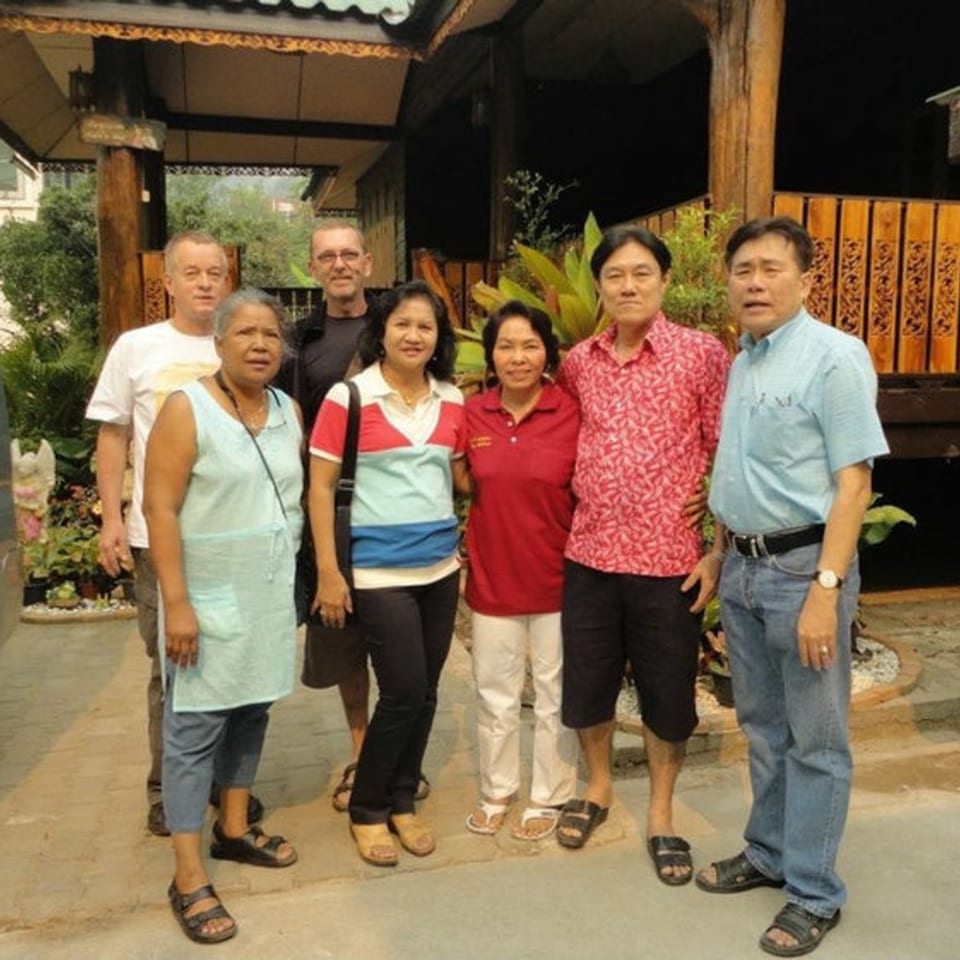 Six adults, three men and three women, stand together outside a Thai restaurant.