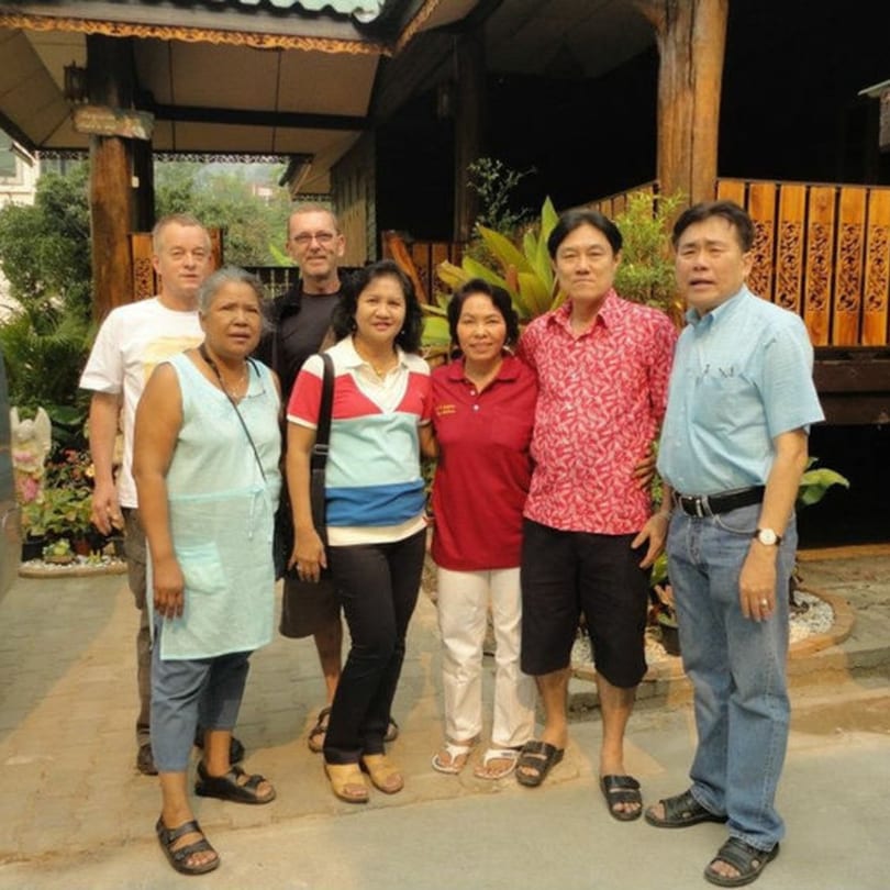 Six adults, three men and three women, stand together outside a Thai restaurant.