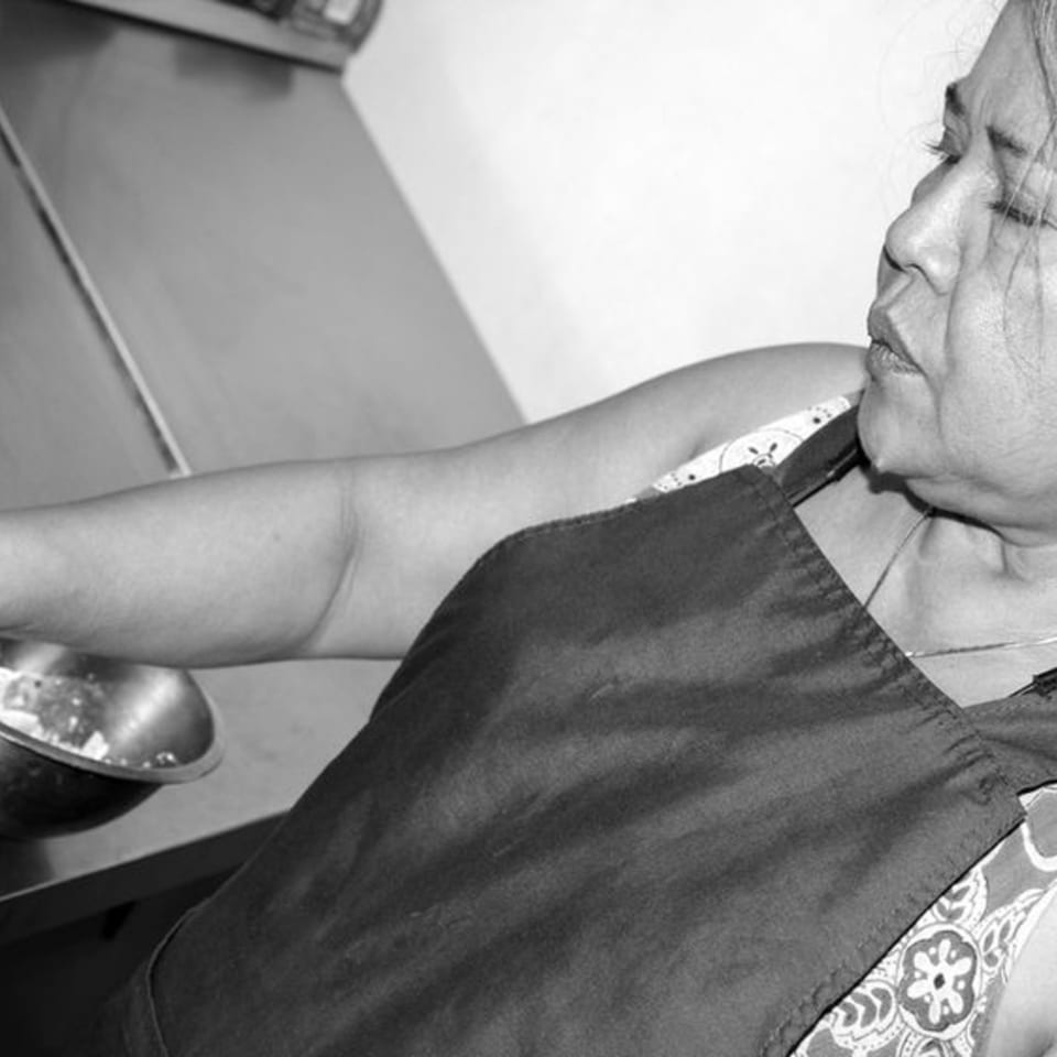A Thai chef in an apron, preparing food in a kitchen, in black and white.