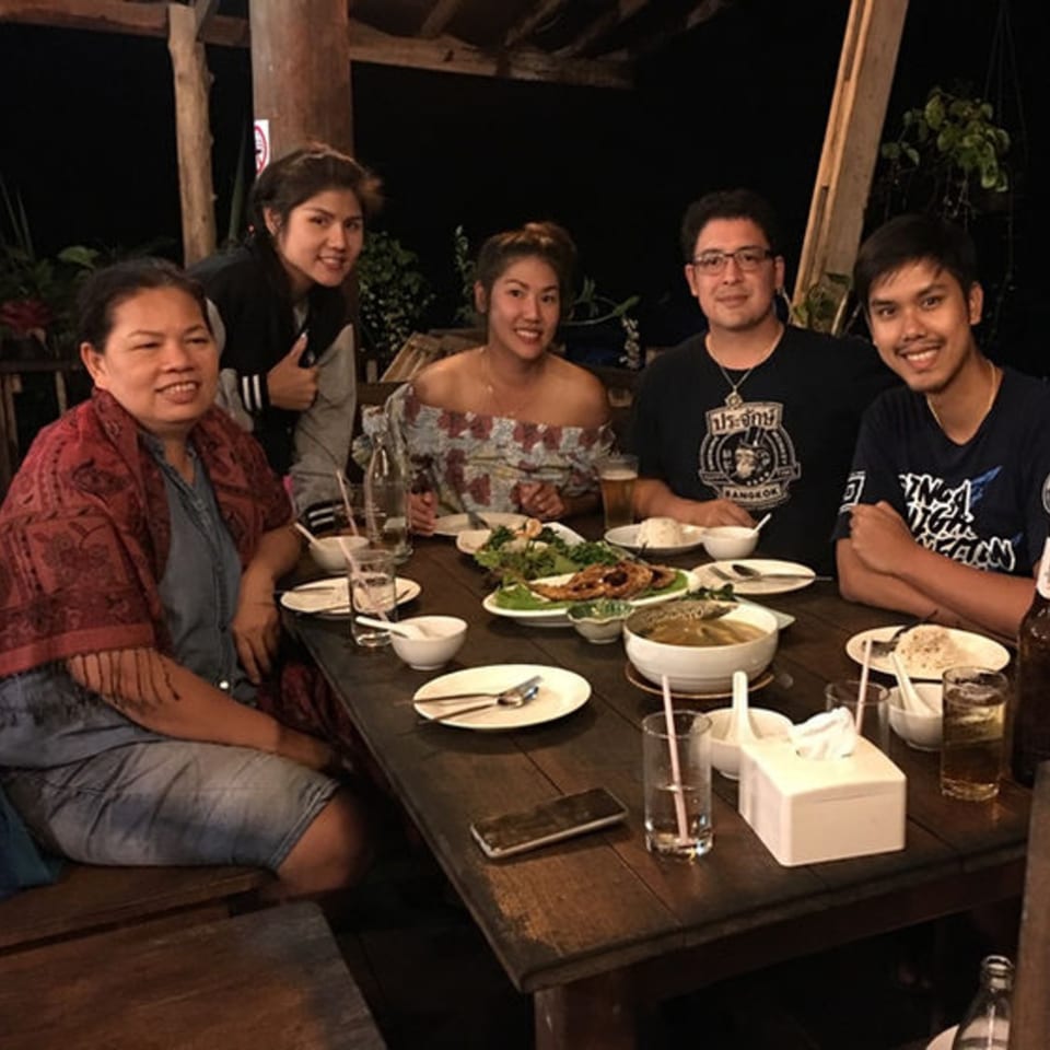 Five people smiling around a table laden with Thai dishes and drinks at Pattaya Thai.