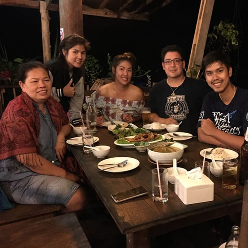 Five people smiling around a table laden with Thai dishes and drinks at Pattaya Thai.