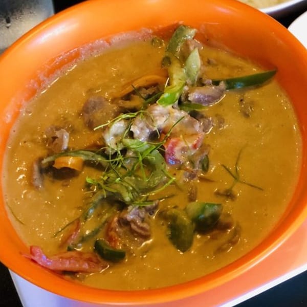 Close-up of a vibrant orange bowl filled with Pattaya Thai green curry, garnished with fresh herbs.