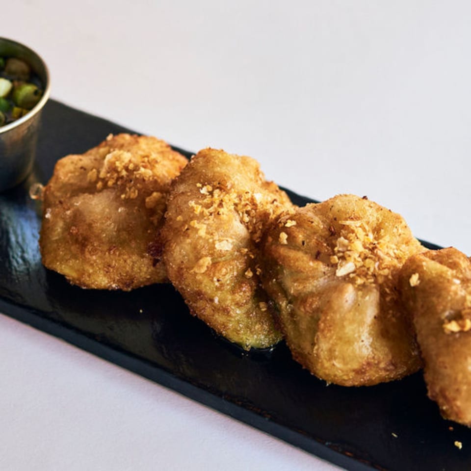 Golden-brown fried Thai dumplings, sprinkled with crushed peanuts, served on a black plate with a dipping sauce.