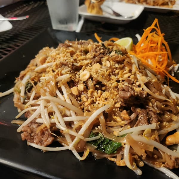 Pattaya Thai's Pad See Ew with beef, wide noodles, bean sprouts, and crushed peanuts on a black plate.