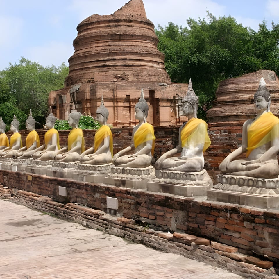 Row of ancient stone Buddha statues with yellow sashes in front of a large brick stupa.