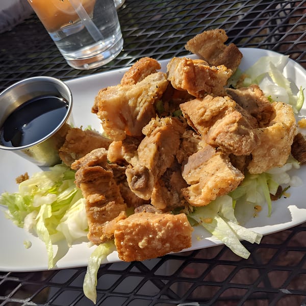 Crispy fried pork belly pieces on a bed of lettuce with a side of dark dipping sauce.