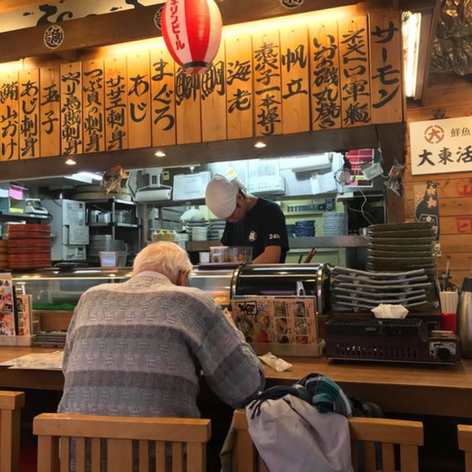 A customer sits at a counter in a Japanese restaurant with a chef working behind it.
